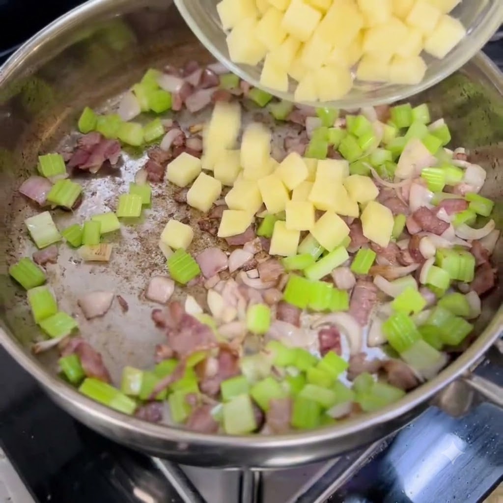Gewürfelte Kartoffeln werden aus einer klaren Schüssel in eine Pfanne mit gehackten Zwiebeln, Sellerie und Speck gefüllt.