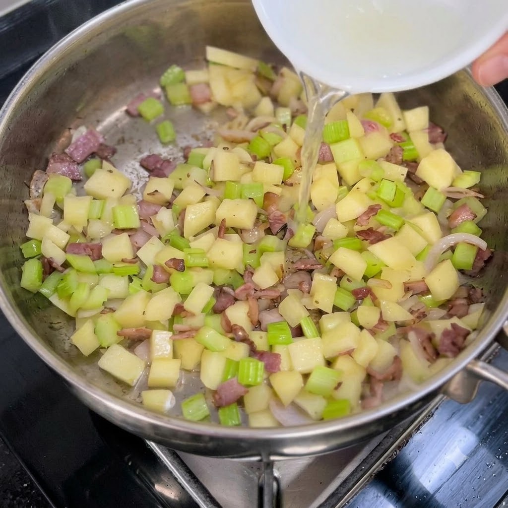 Klares Muschelbrühe wird aus einer weißen Schüssel in eine Pfanne mit sautiertem Gemüse und Speck gegossen.