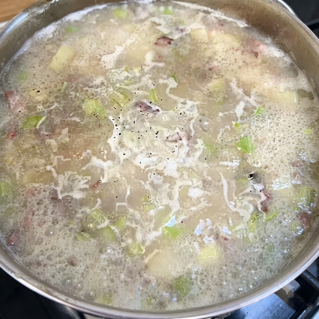 Ein Topf mit köchelnder Chowder-Basis, auf deren blubbernder Oberfläche schwarzer Pfeffer zu sehen ist.