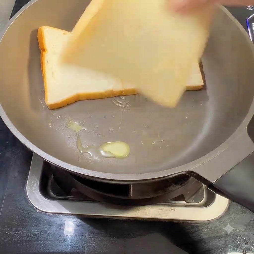 Drei Scheiben weißes Toastbrot werden in eine gebutterte Bratpfanne gelegt.