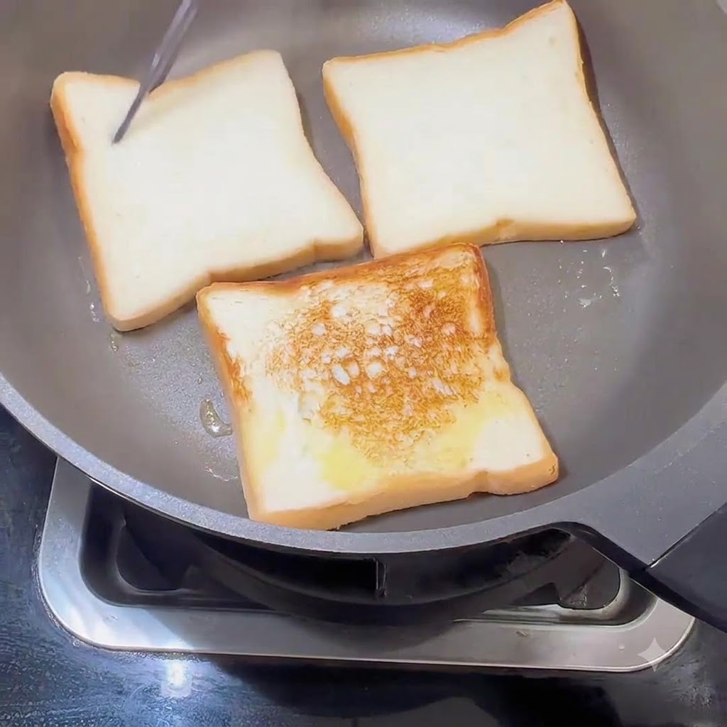 Brotscheiben werden in einer Pfanne gewendet und zeigen eine goldbraune Toastkruste auf einer Seite.