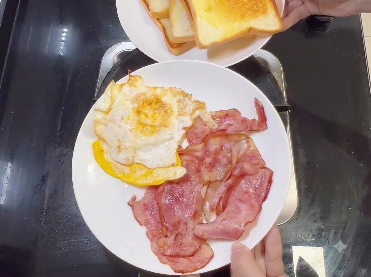 Ein weißer Teller mit gebratenem Speck und Spiegeleiern, darüber ein weiterer Teller mit getoastetem Brot.