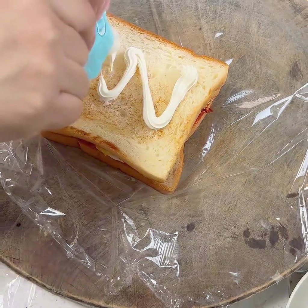 Mayonnaise wird in einem Zickzackmuster auf eine Scheibe Toastbrot gespritzt.