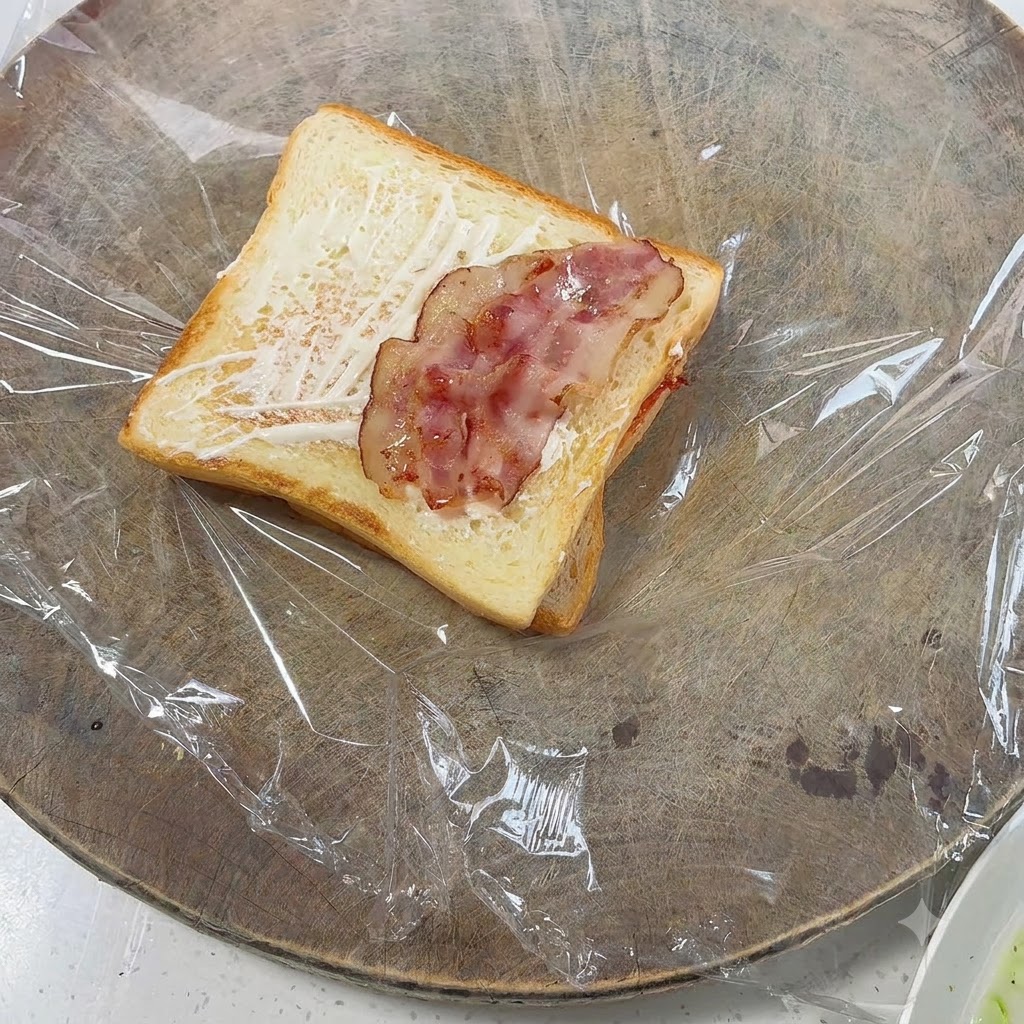 Stücke von gebratenem Speck sind auf dem getoasteten Brot ausgelegt.