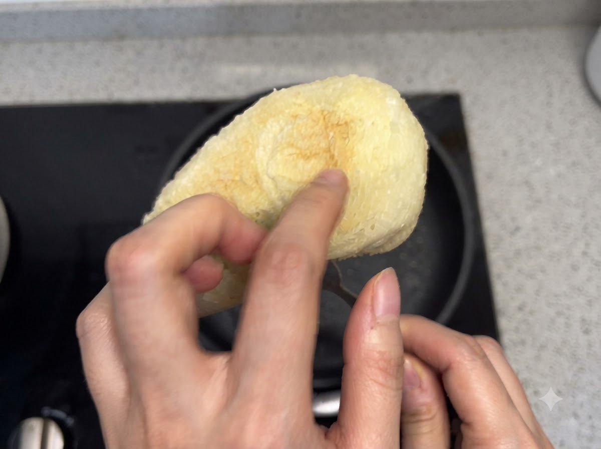 Eine Hand drückt auf die Unterseite eines gerösteten Brotstücks, um dessen Knusprigkeit zu prüfen.