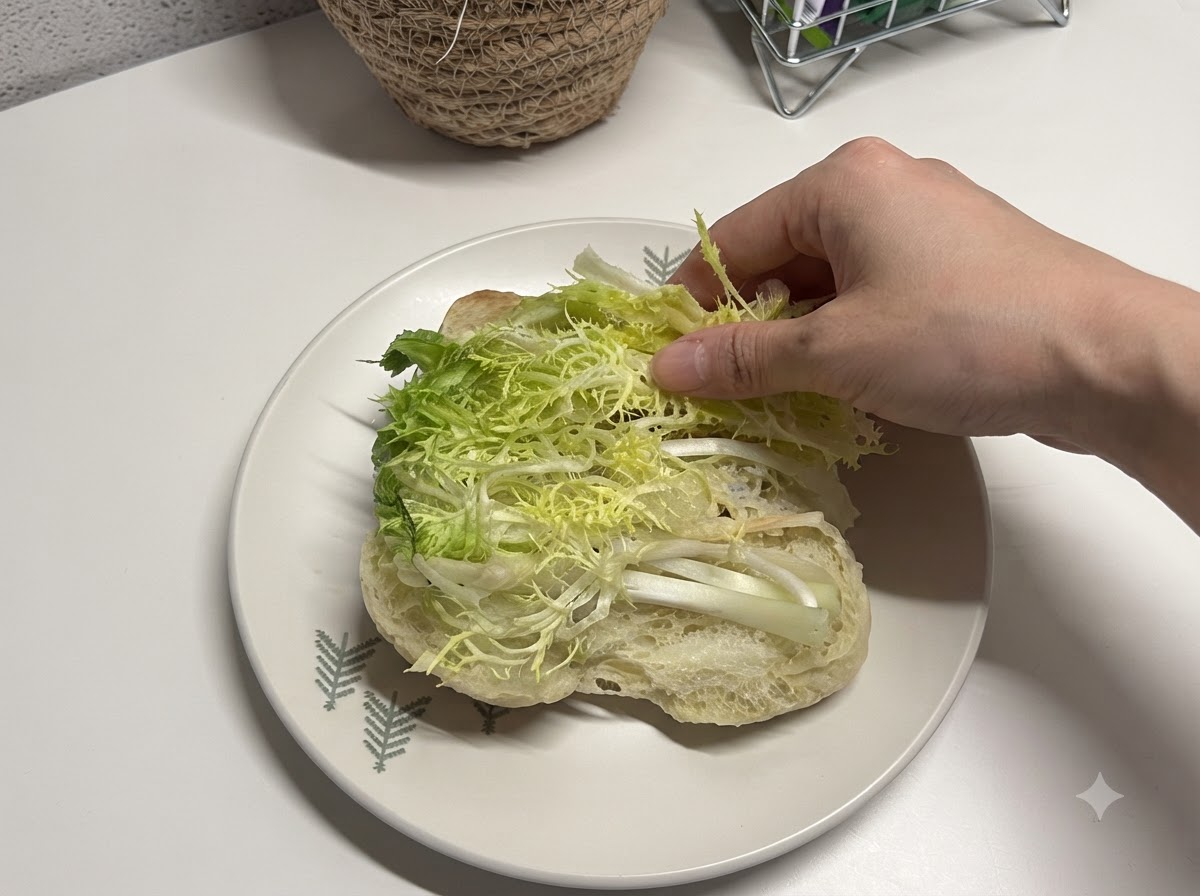 Frischer, geschnittener Salat wird in ein geöffnetes Ciabattabrot gelegt.