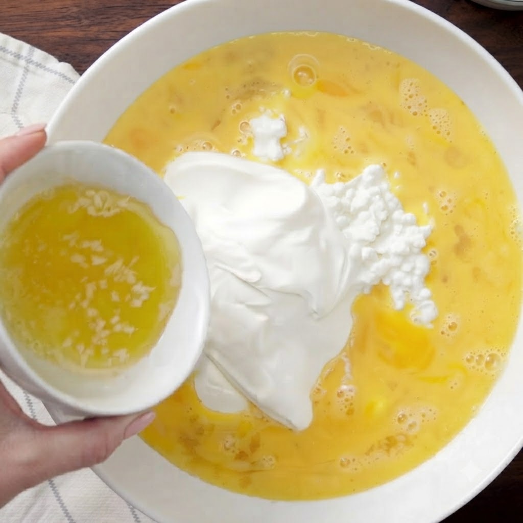 Geschmolzene Butter wird aus einer kleinen weißen Schüssel in die Rührschüssel gegossen.