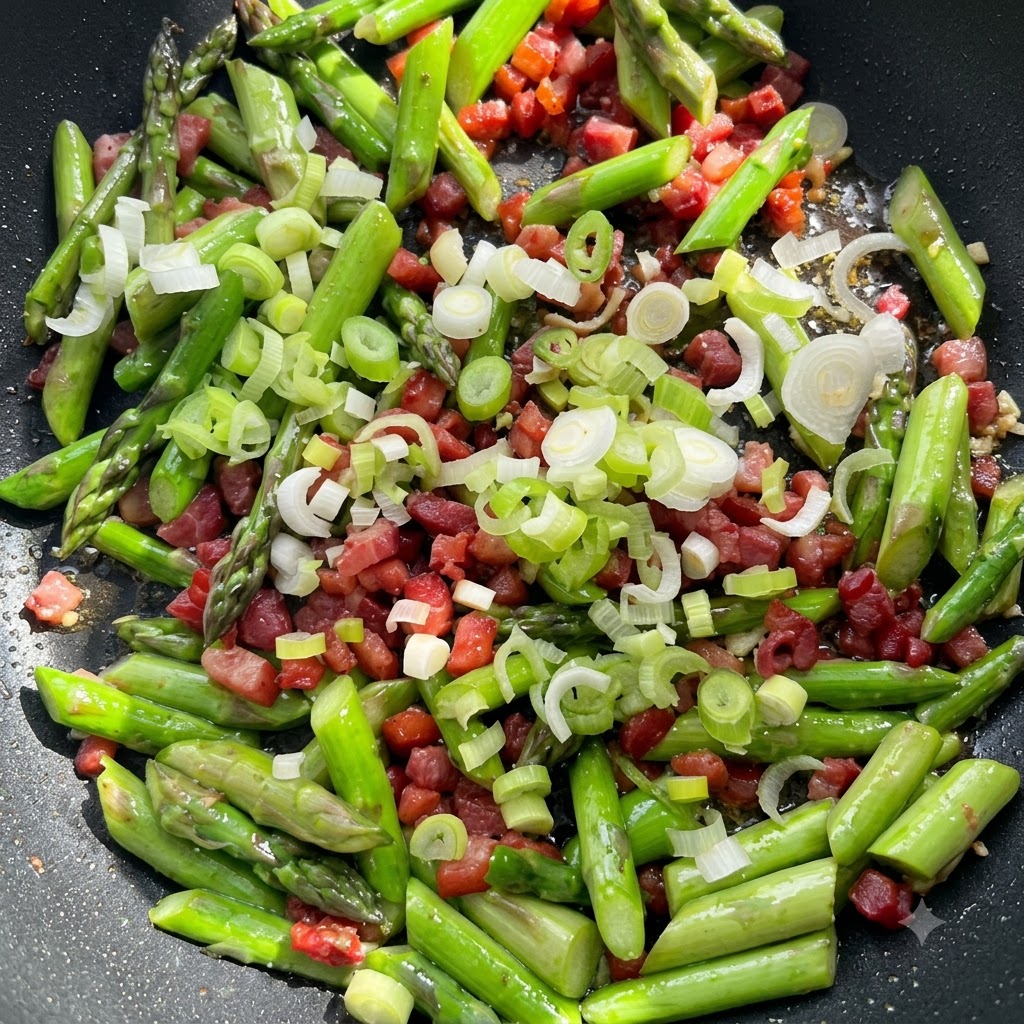 Fein gewürfelter Knoblauch und Frühlingszwiebelweiß, verteilt auf Spargel und Speck in der Pfanne.