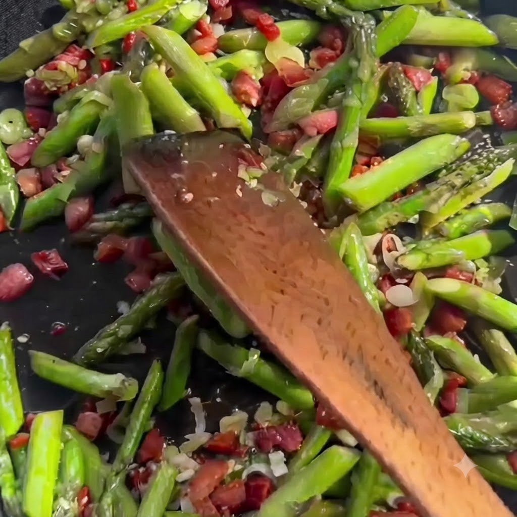 Klare Flüssigbrühe wird aus einem Behälter in eine zischende Pfanne mit geschnittenem grünem Spargel und Speckstücken gegossen.