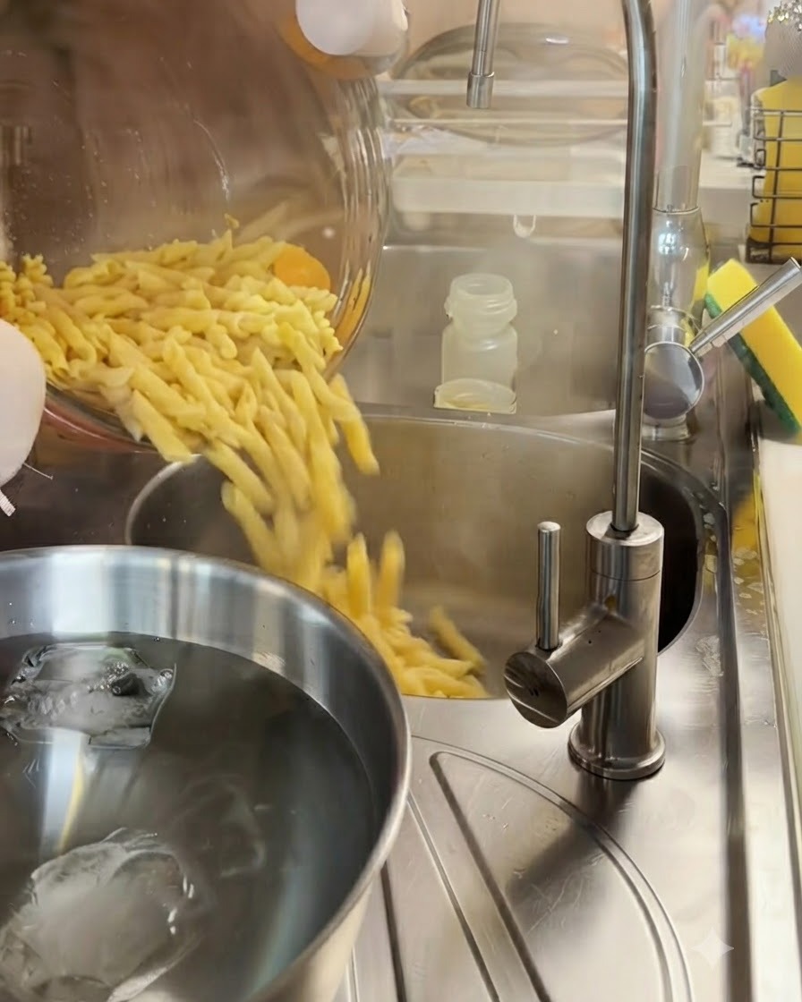 Gekochte Fusilli Pasta wird in einem Metall-Seiher über einer Schüssel mit Eiswasser abgegossen.