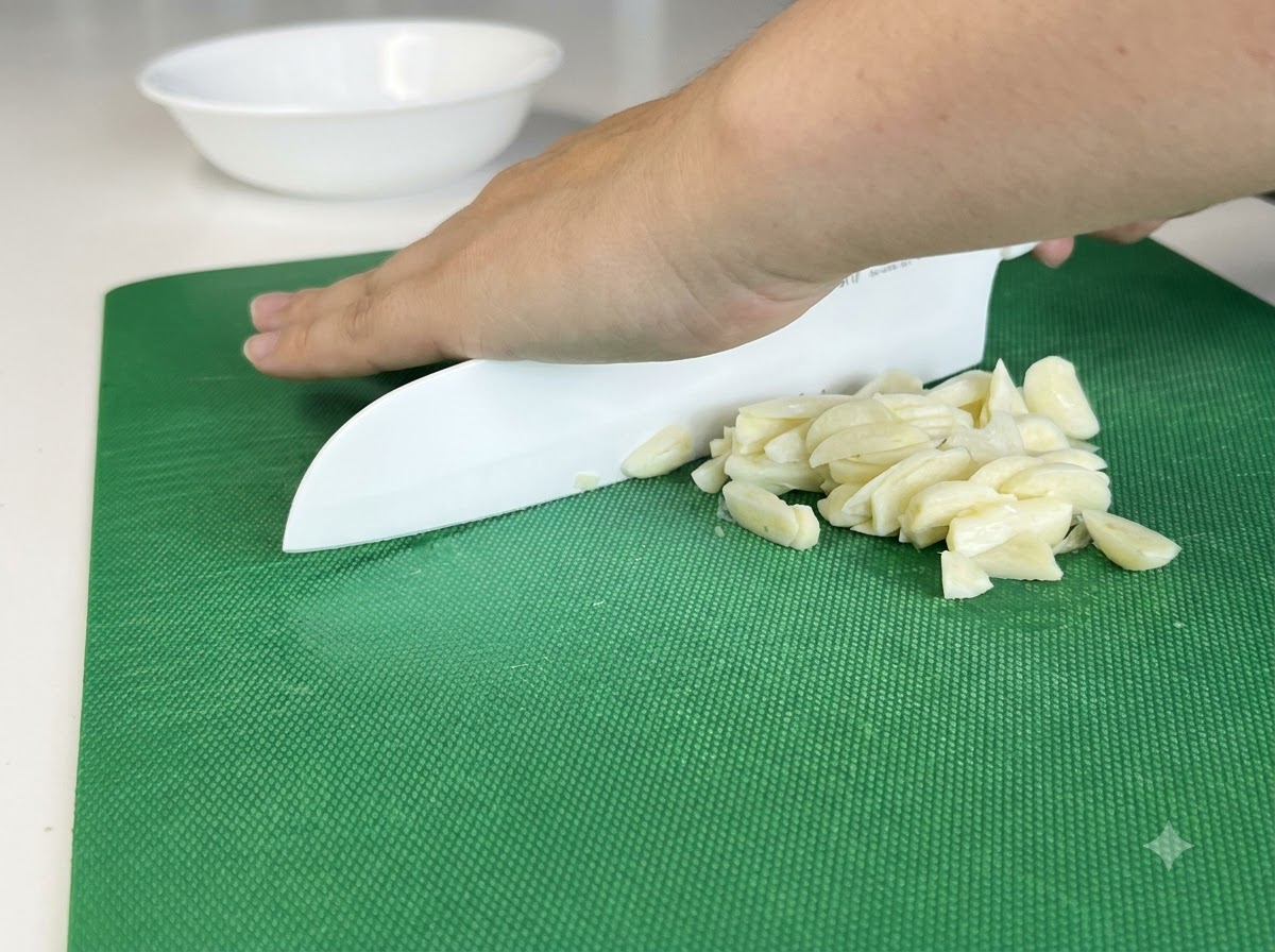 Knoblauchzehen werden auf einem grünen Schneidebrett mit einem weißen Messer fein gehackt.
