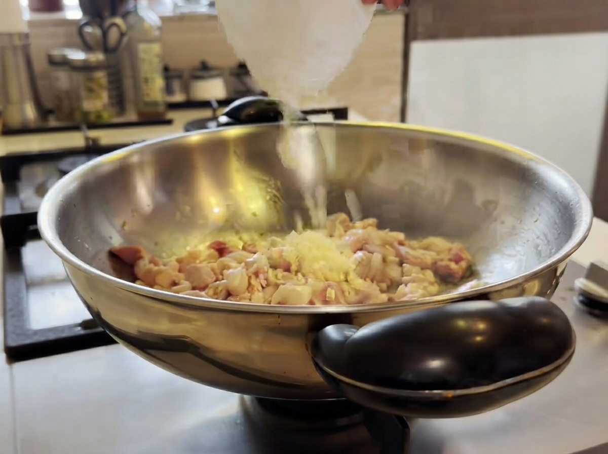 Gehackter Knoblauch wird in einen Wok mit kochendem Hähnchen gegeben und mit einem Spatel umgerührt.