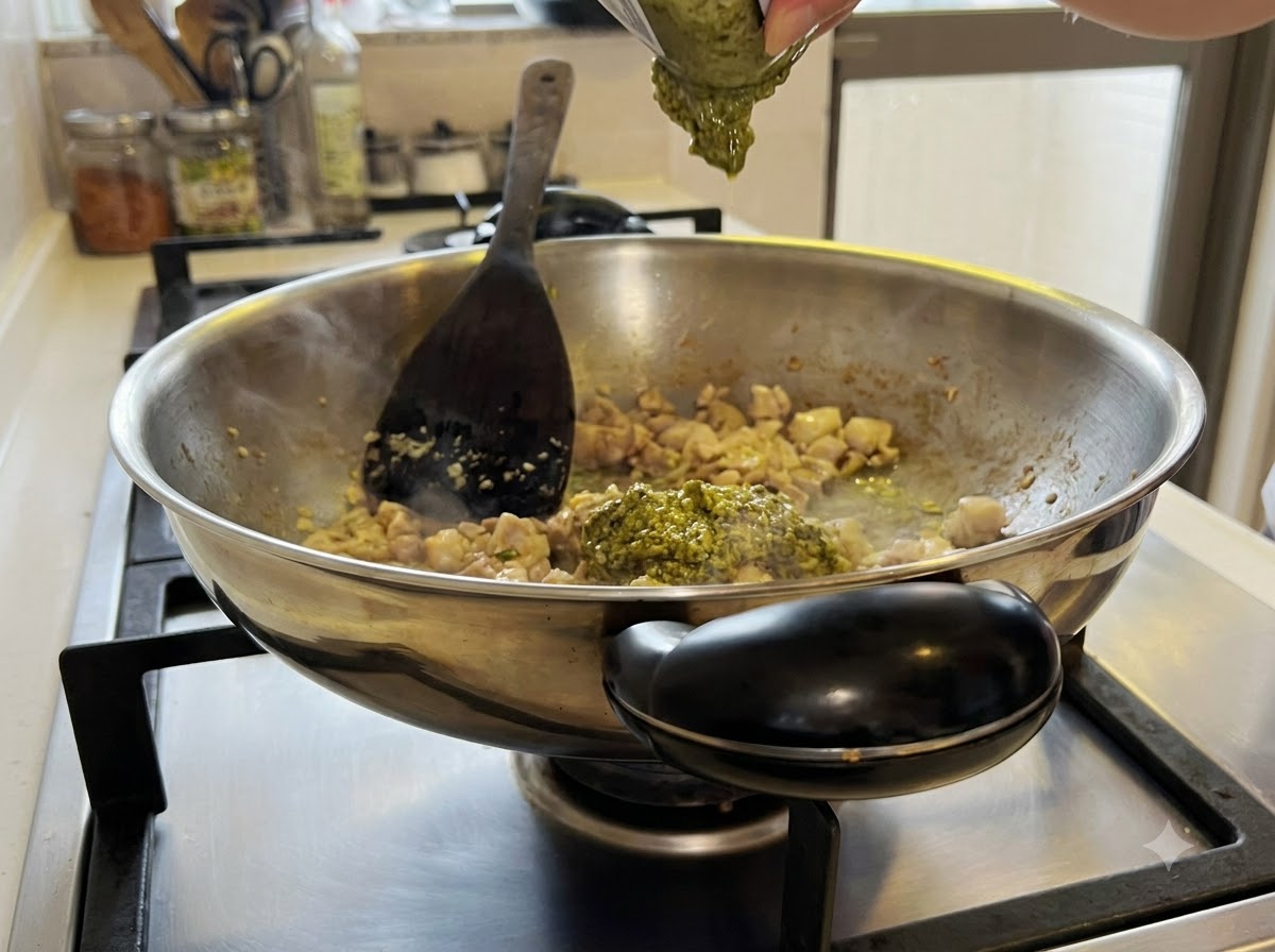 Grüne Pestosoße wird im Wok unter die Hähnchen-Knoblauch-Mischung gemischt.