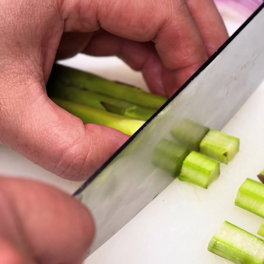 Geschälte grüner Spargelstangen werden mit einem Chefkochmesser in kleine, gleichmäßige Stücke geschnitten.