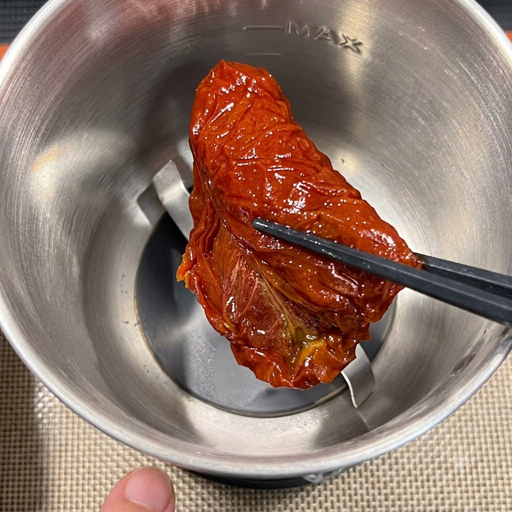 Ein einzelnes Stück getrocknete Tomate wird mit Essstäbchen in einen Edelstahl-Mixerbehälter gegeben.