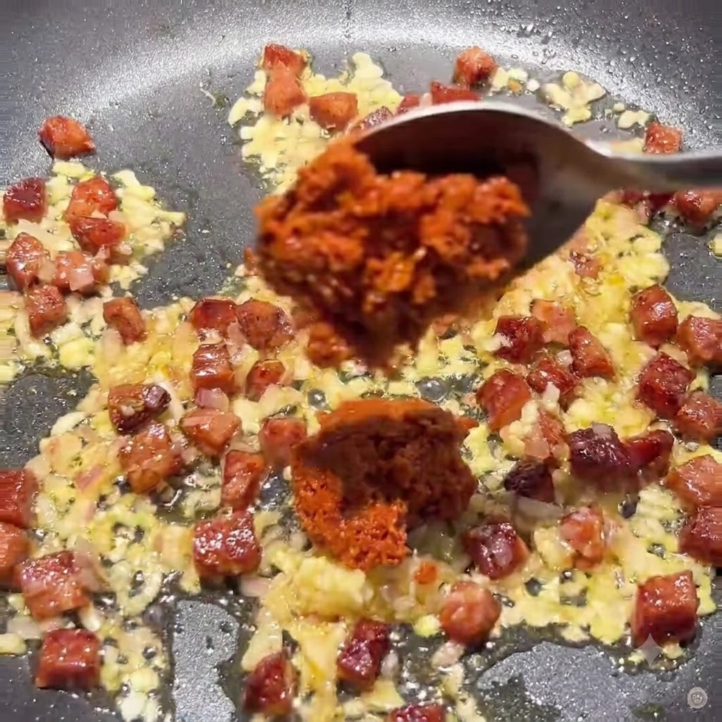 Ein Löffel gibt dicke getrocknete Tomatenpaste und Tomatenmark in die Pfanne mit der Chorizo-Zwiebel-Mischung.