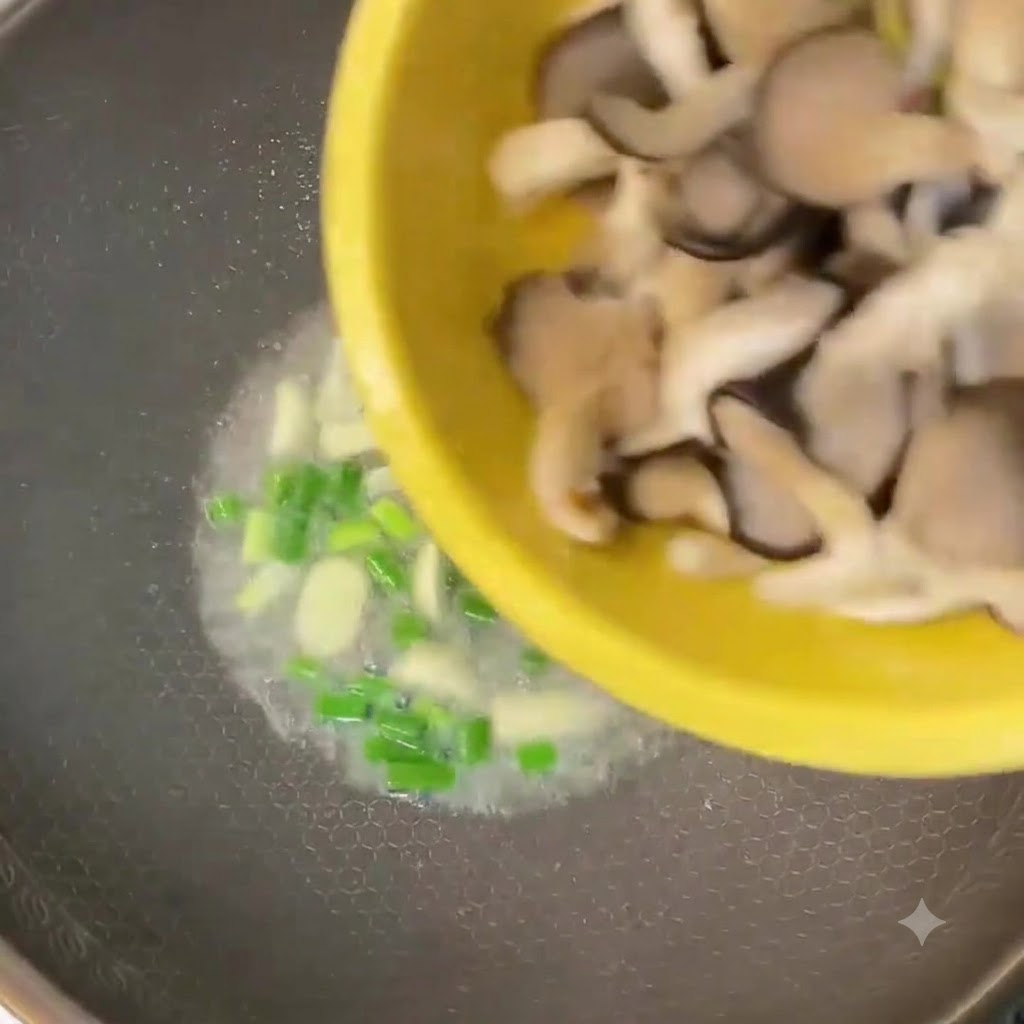 Gehackte Austernpilze werden aus einer gelben Schüssel in einen Wok mit Lauchzwiebeln und Knoblauch gegeben.
