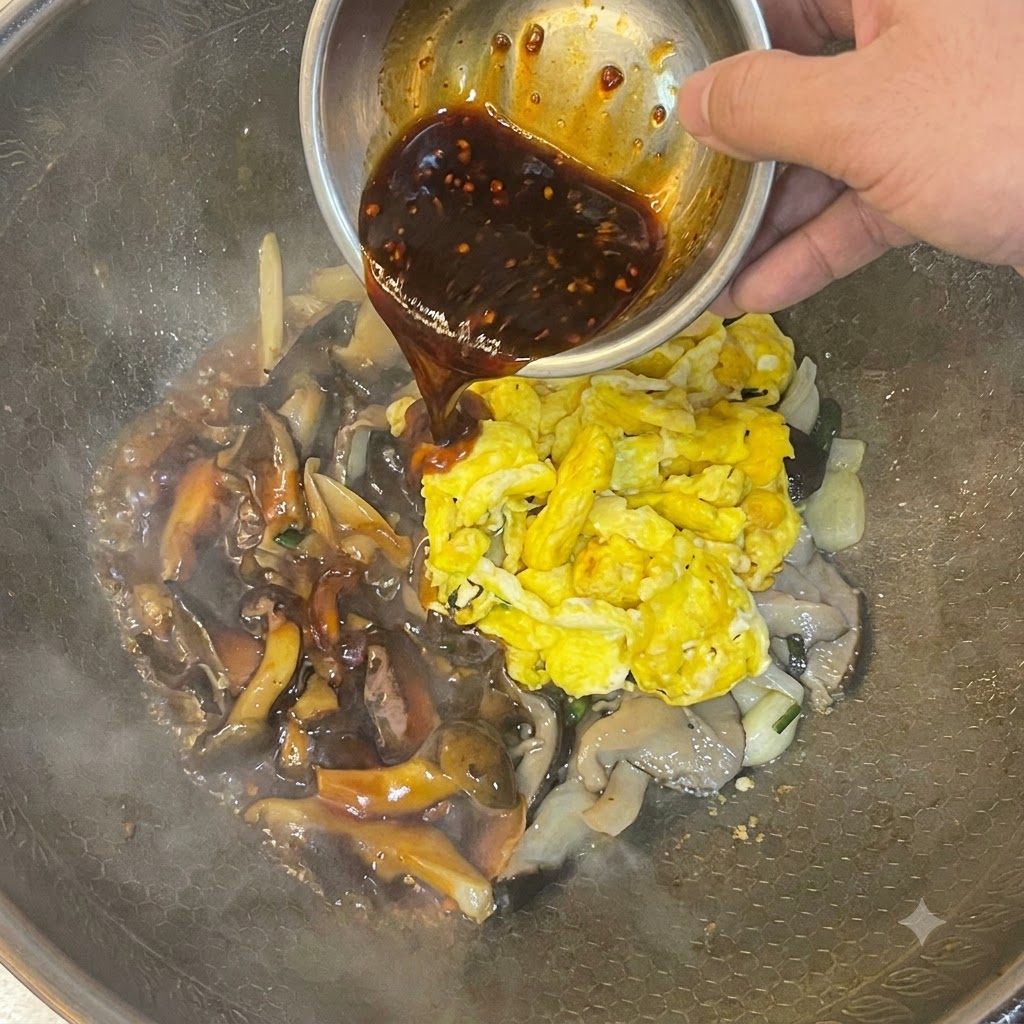 Dunkle Sauce wird aus einer Metallschnalle über Rührei und Pilze in einem Wok gegossen.