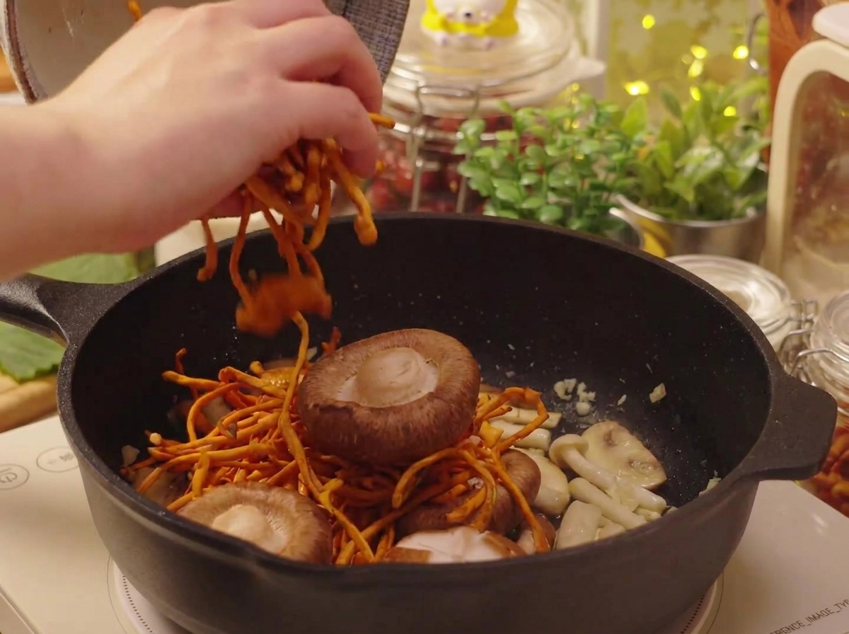 Eingeweichte Shiitake-Pilze und Cordyceps werden in die Pfanne gegeben.