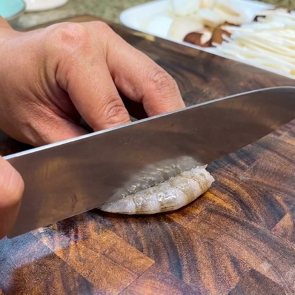 Rohgarnelen werden auf einem Holzschneidebrett mit einem Messer gereinigt und entdarmt.