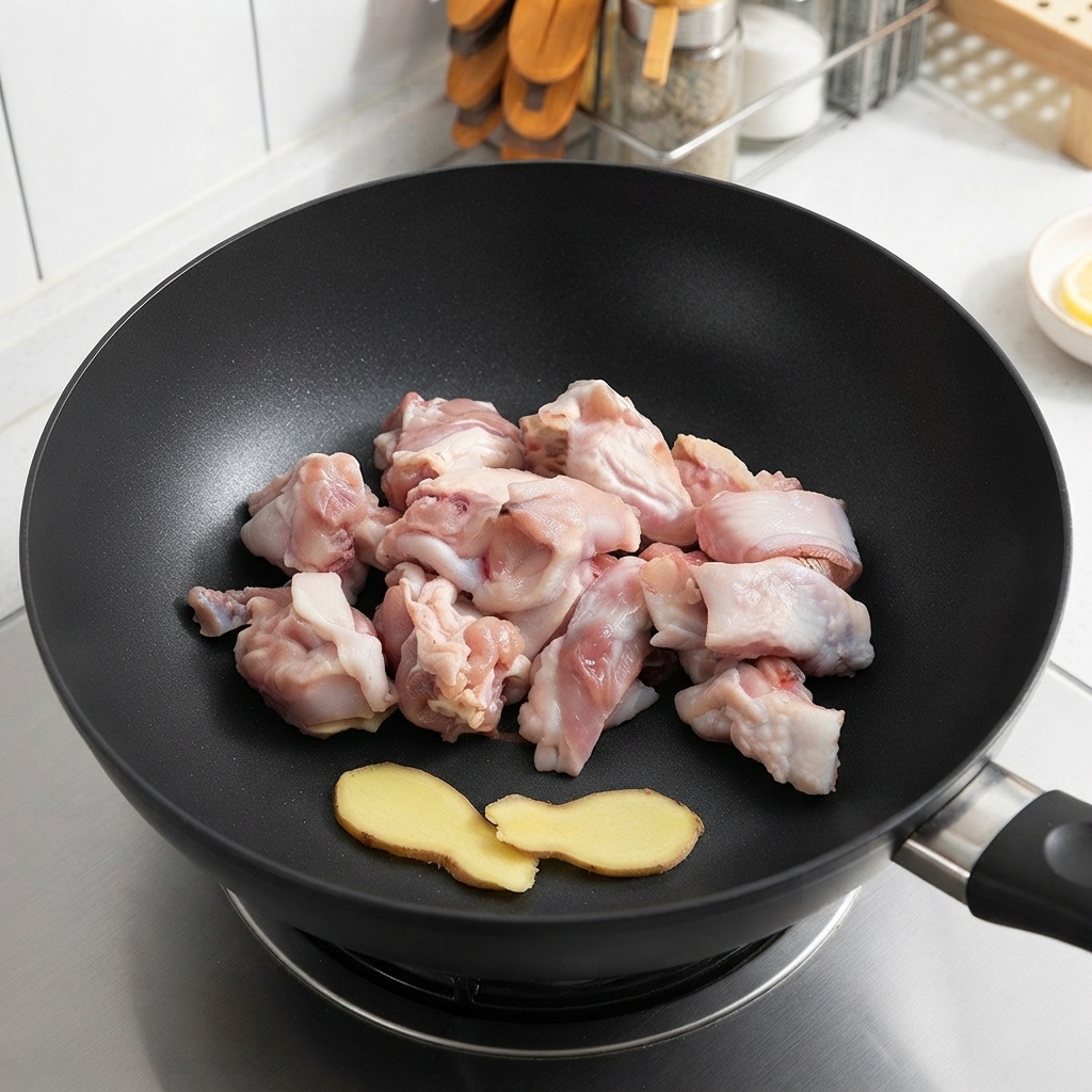 Rohe Hähnchenstücke und Ingwerscheiben liegen vor dem Braten in einem Wok.