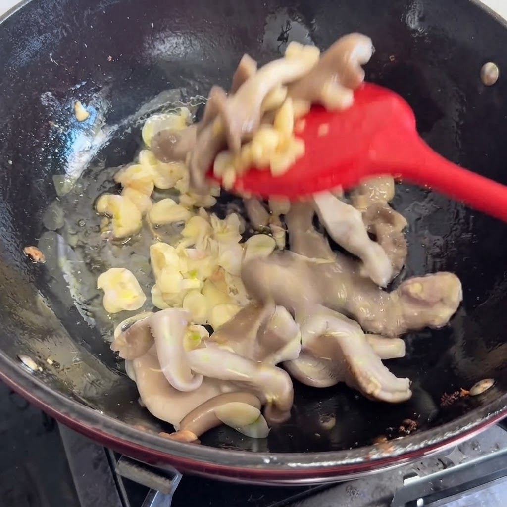 Frische Pilze werden mit einem roten Spatel in die Pfanne zu den Aromen gegeben und umgerührt.