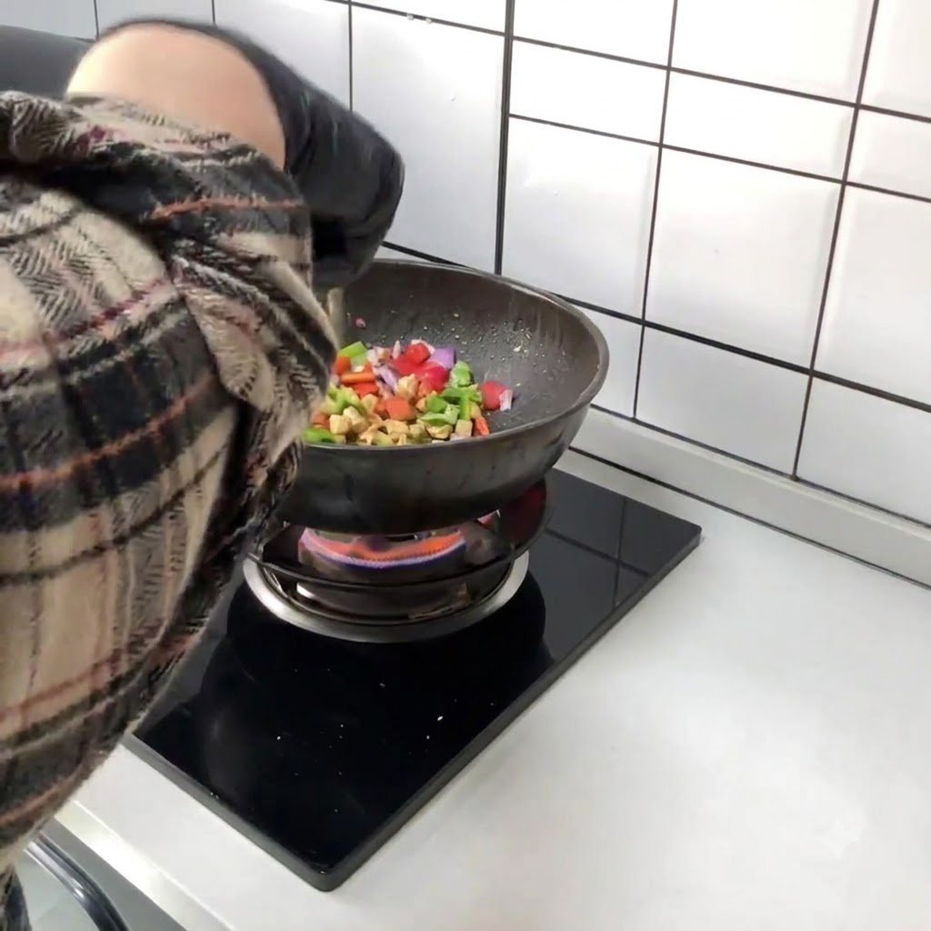 Gehackte rote und grüne Paprika werden direkt in den Wok mit dem angebratenen Hähnchen gegeben.
