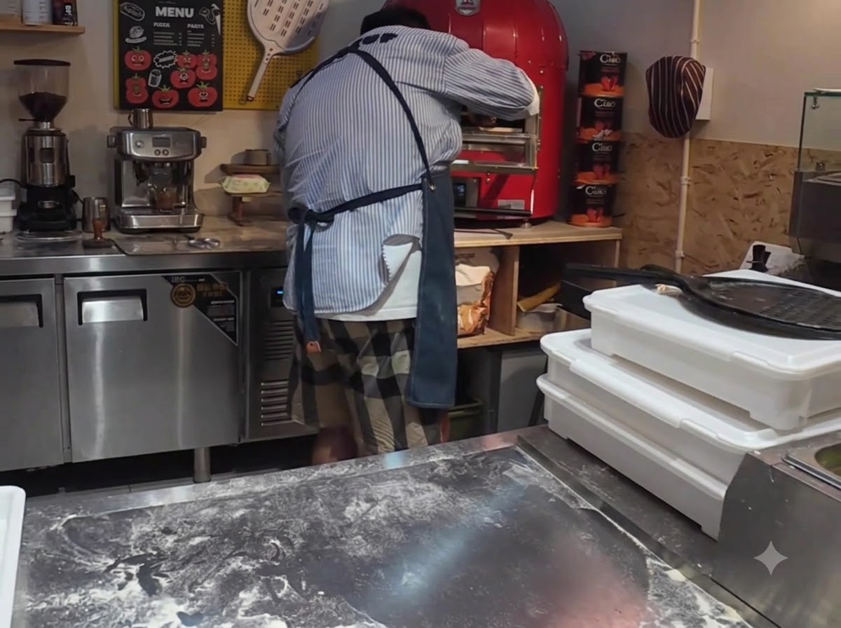 Eine Pizza wird mit einem Pizzaschieber in einen leuchtend roten gewerblichen elektrischen Pizzaofen geladen.