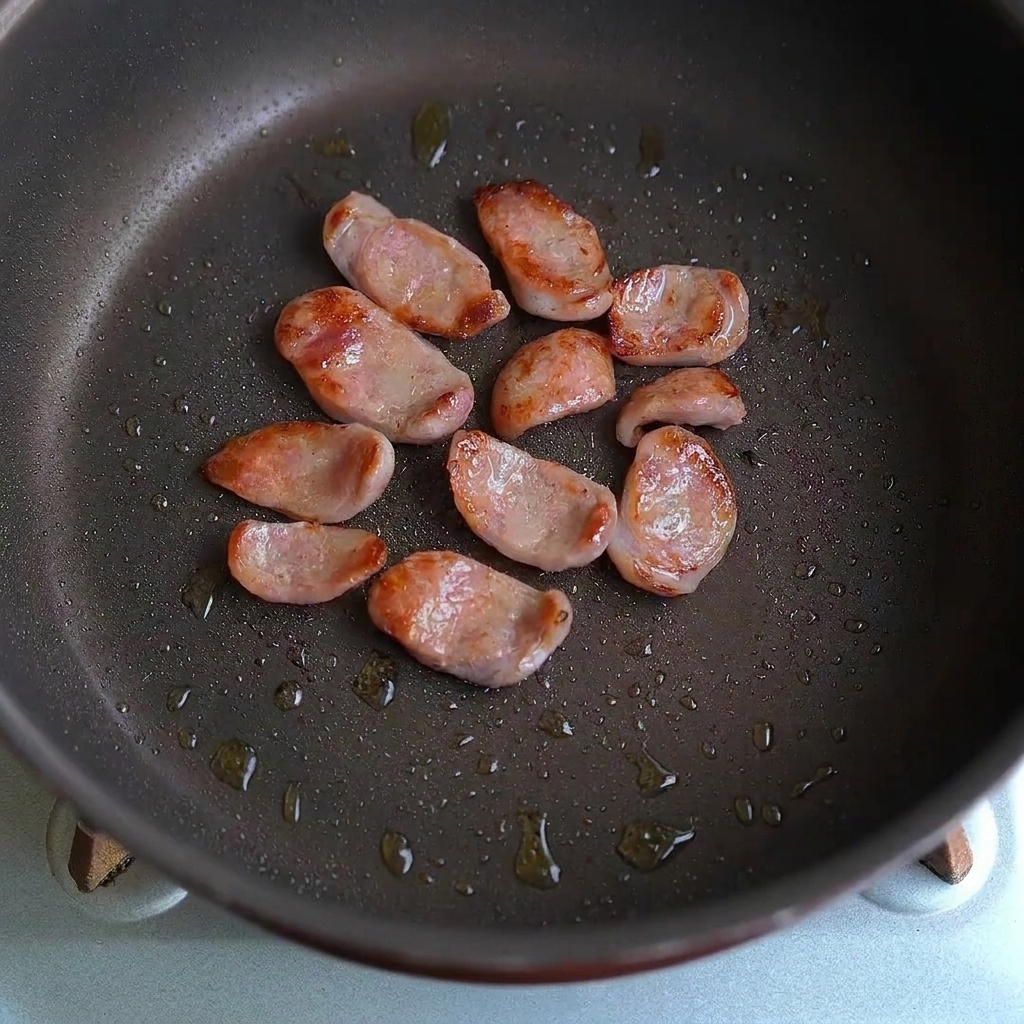 Wurstscheiben und Knoblauchstücke werden in einer Bratpfanne zusammen geschwenkt.