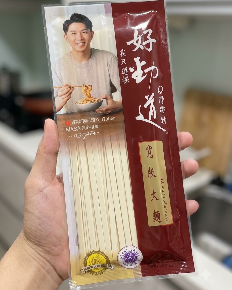 Eine Packung Hao Jin Dao Bandnudelstäbchen vor einem Küchenhintergrund gehalten.