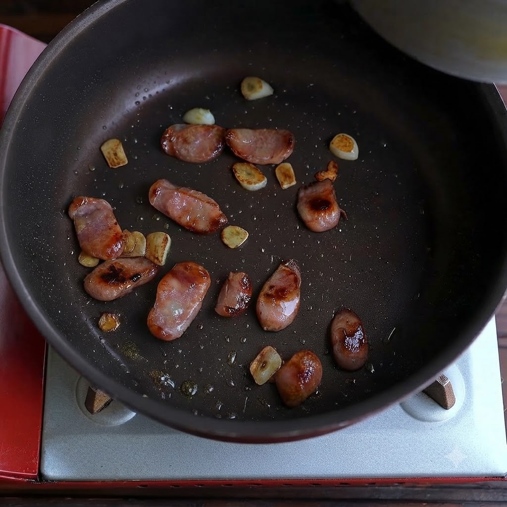 Gekochte Wurst und gebratene Knoblauchstücke verstreut am Boden einer Bratpfanne.