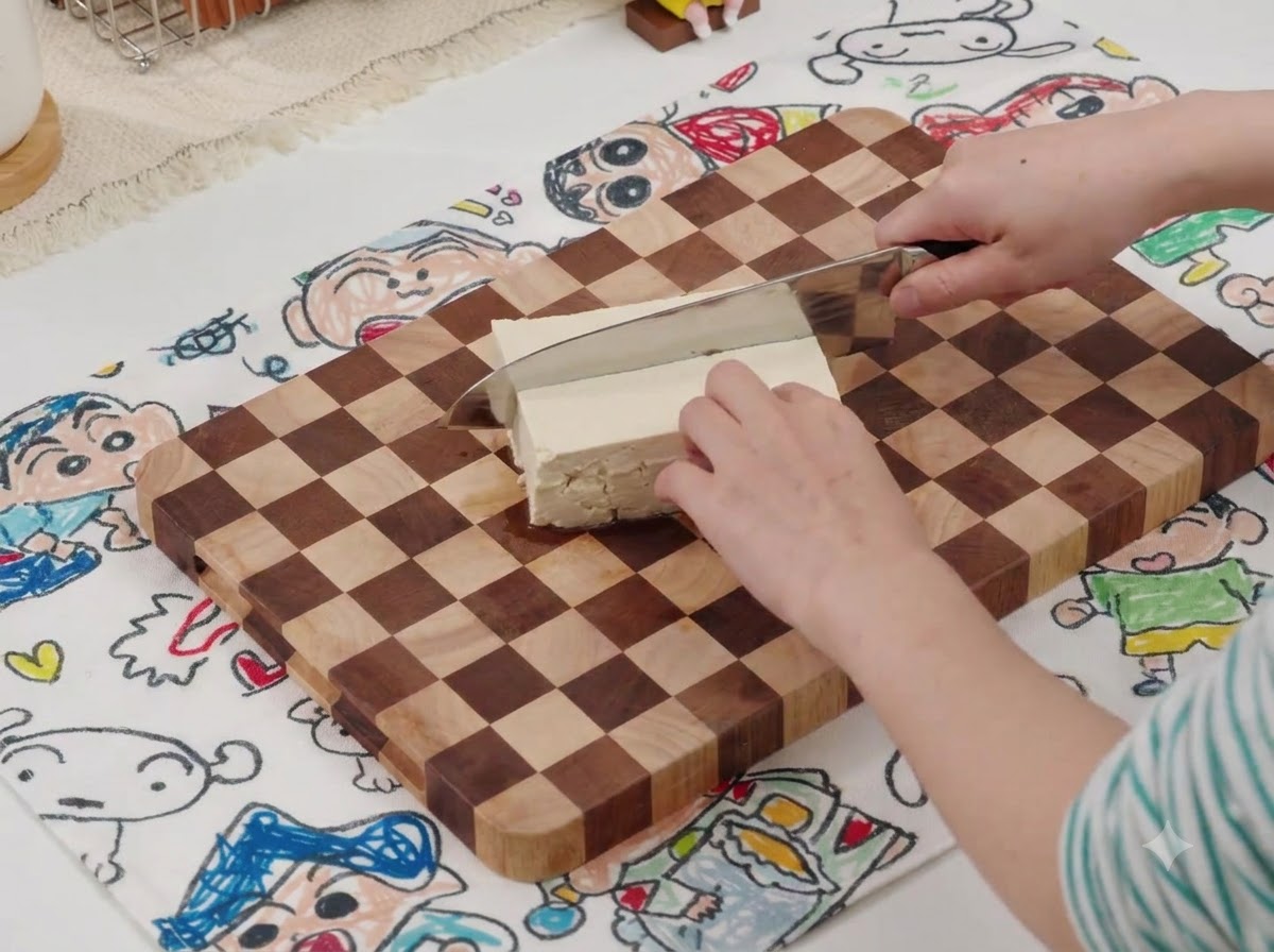 Ein Messer schneidet einen Block weißen Tofu auf einem Holzschneidebrett.