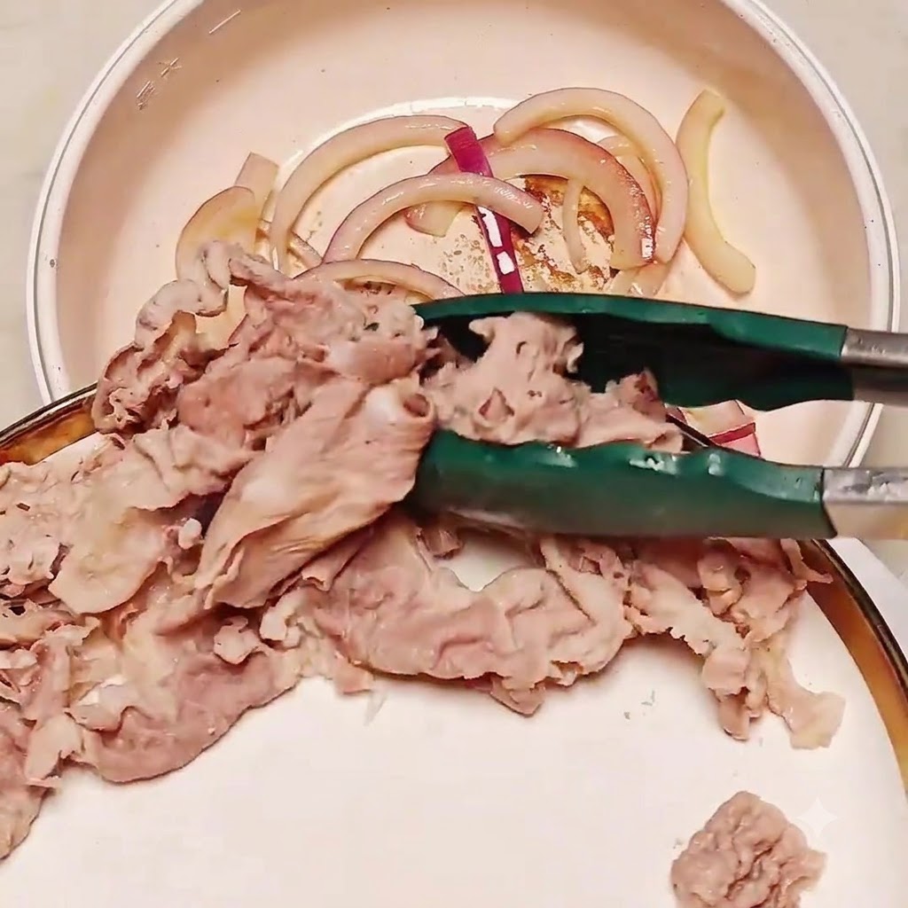 Blanchierte Rindfleischscheiben werden mit einer Zange in eine Pfanne mit angebratenen Zwiebeln gegeben.