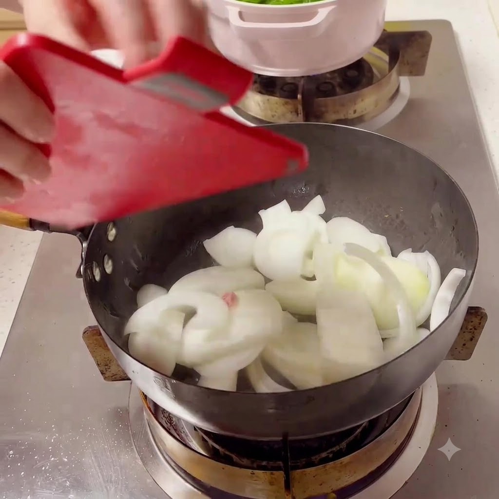 Weiße Zwiebelscheiben werden von einem roten Schneidebrett in einen heißen schwarzen Wok auf dem Herd gegeben.