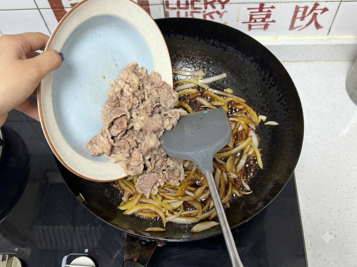 Vorgeblanchierte Rindfleischstreifen werden von einem Teller in einen Wok mit Zwiebeln und dunkler Soße gegeben.