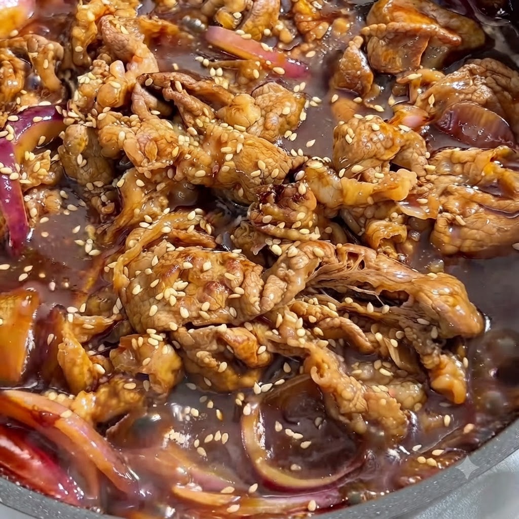 Nahaufnahme von gekochtem Rindfleisch und roten Zwiebeln in dunkler, herzhafter Sauce, bestreut mit weißen Sesamsamen.