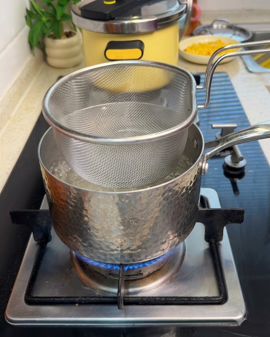Ein Siebkorb mit Rindfleischscheiben hängt in einem Topf mit kochendem Wasser auf dem Herd.
