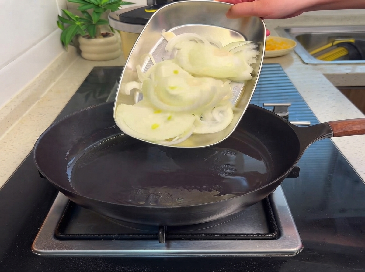 Geschnittene Zwiebeln werden von einem Metalltablett in eine heiße Pfanne mit Öl gegeben.