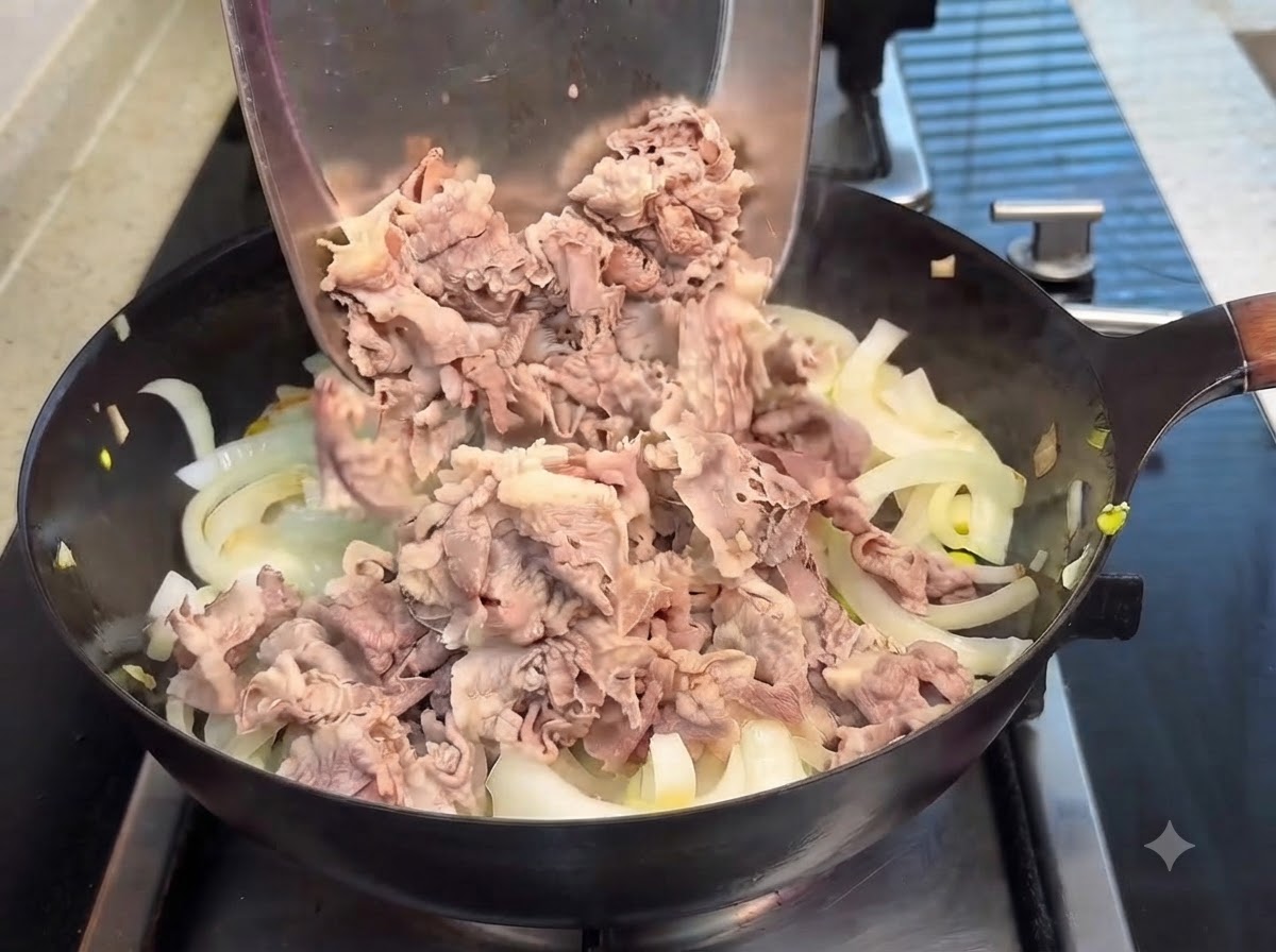 Blanchierte Rindfleischscheiben werden mit einem Pfannenwender in eine Pfanne mit durchscheinenden Zwiebeln gegeben, während Teriyaki-Sauce darüber gegossen wird.