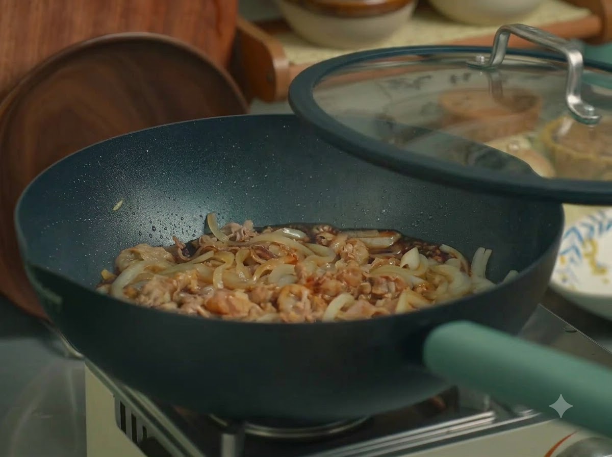 Eine Pfanne mit Rindfleisch und Zwiebeln, die mit einem Glasdeckel abgedeckt auf dem Herd steht.