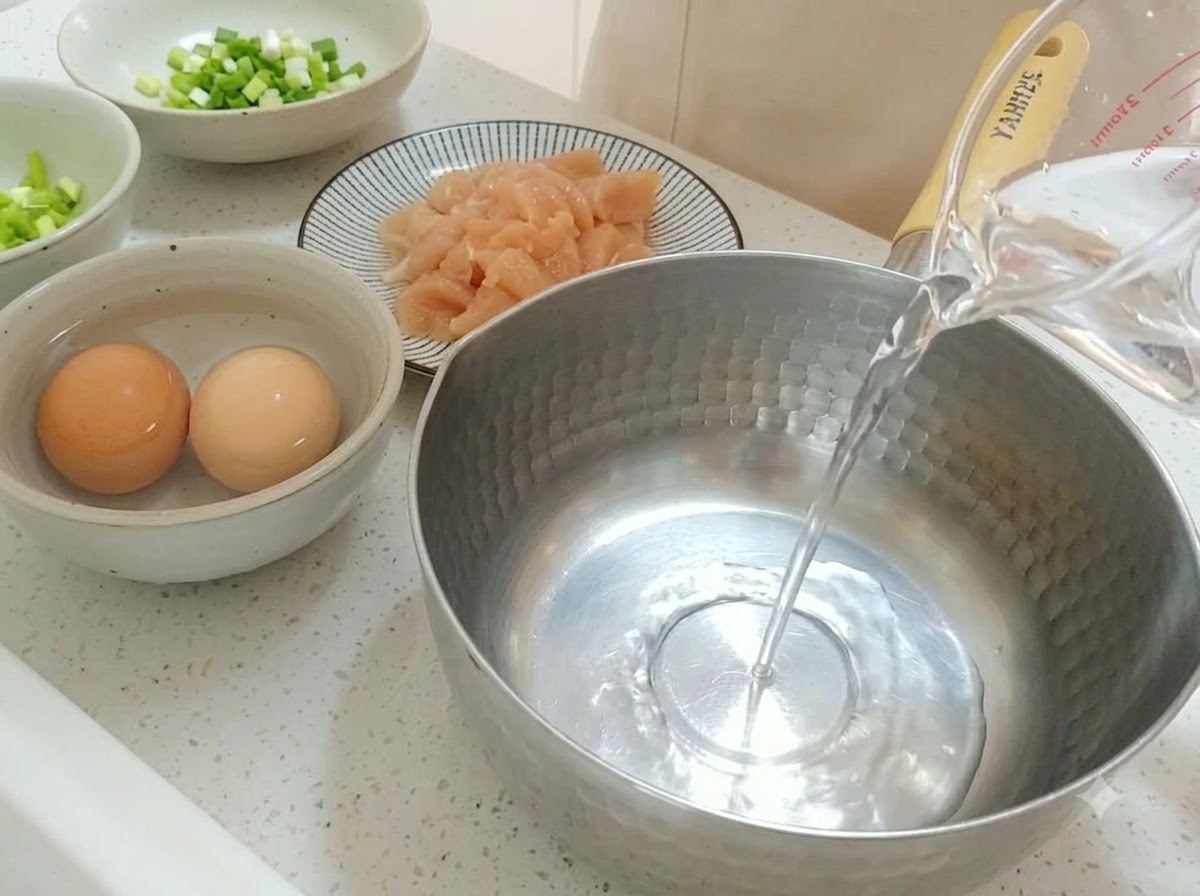 Klares Wasser wird aus einem Messbecher in einen Edelstahltopf gegossen.