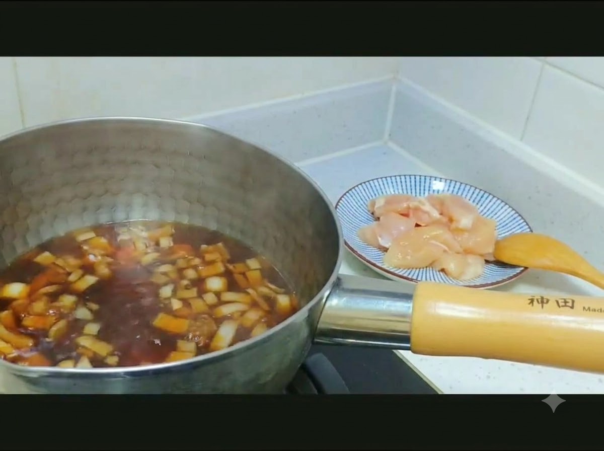 Rohes, gewürfeltes Hähnchenfleisch und geschnittene Zwiebeln werden von einem Teller in einen Topf mit dunkler Brühe gegeben.