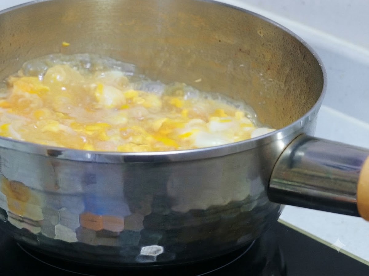Teilweise verquirlte Eimasse wird über köchelndes Hähnchen und Zwiebeln in einem Topf gegossen.