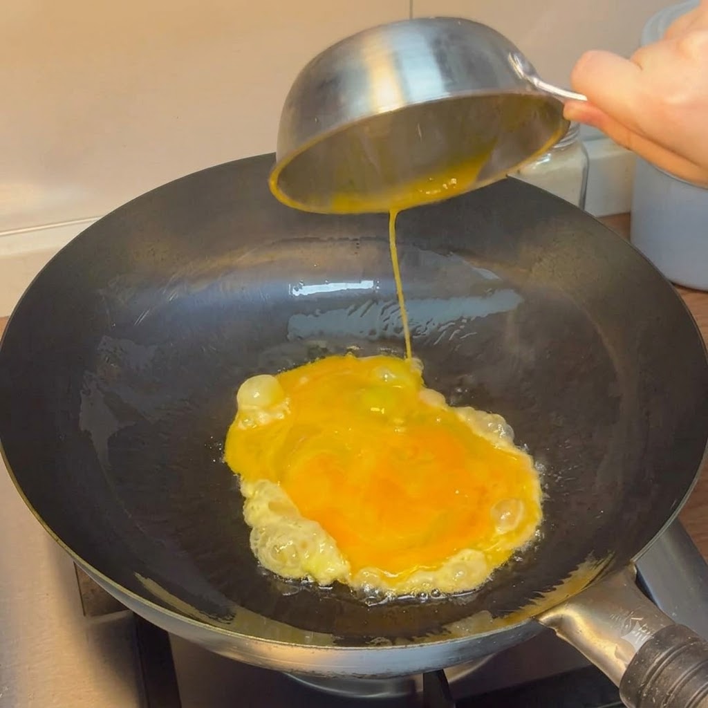 Verquirlte Eier werden aus einer Stahlschüssel in einen heißen WOK gegossen.