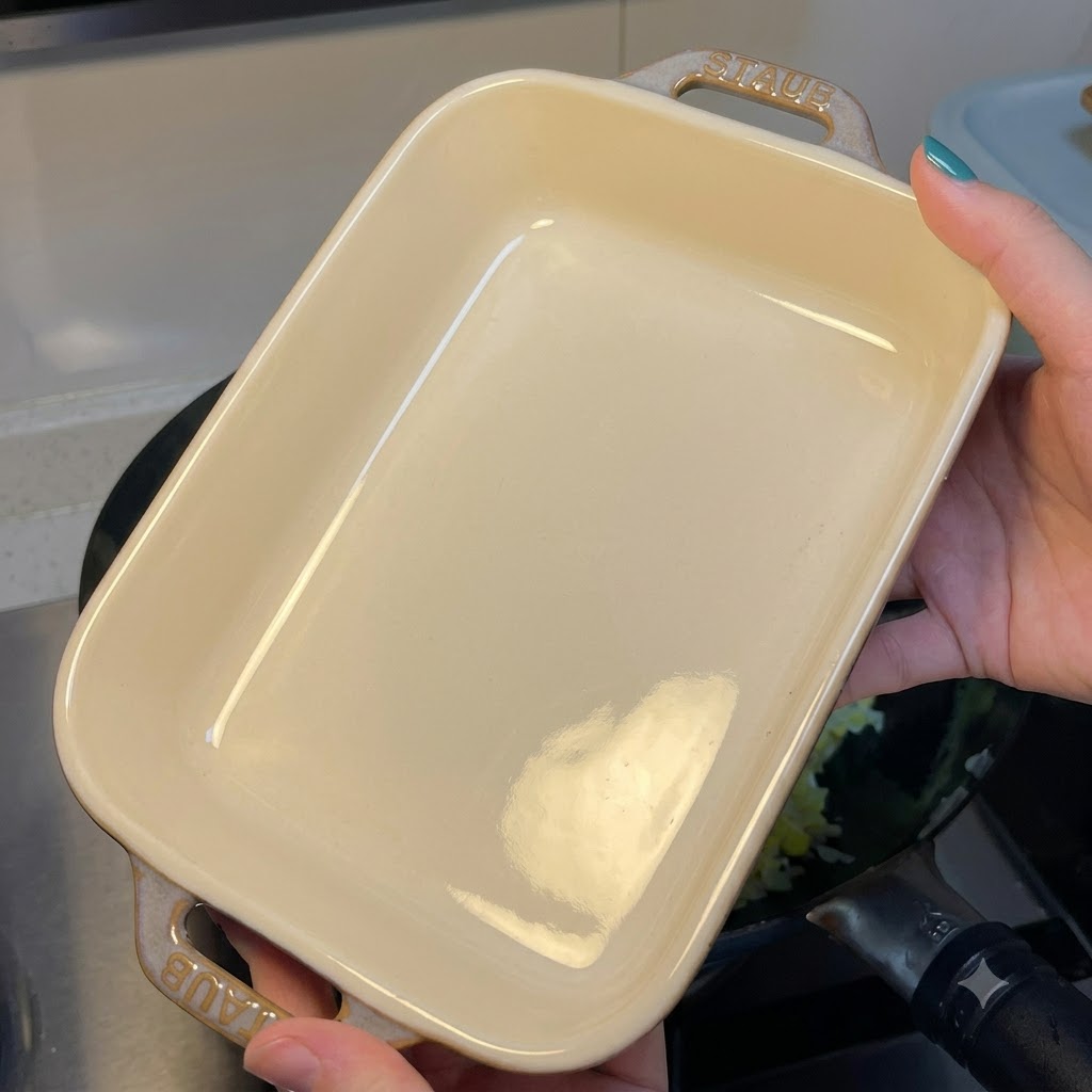 Eine Person hält eine leere rechteckige weiße Keramik-Auflaufform über einen Wok mit Eierbratreis.