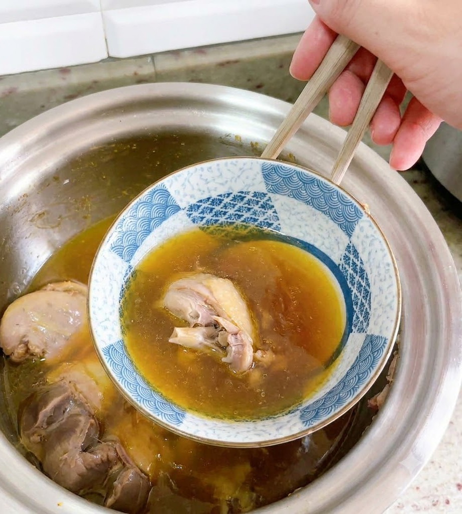 Eine umgedrehte Keramikschüssel wird vorsichtig mit Stäbchen aus der Entensuppe gehoben.