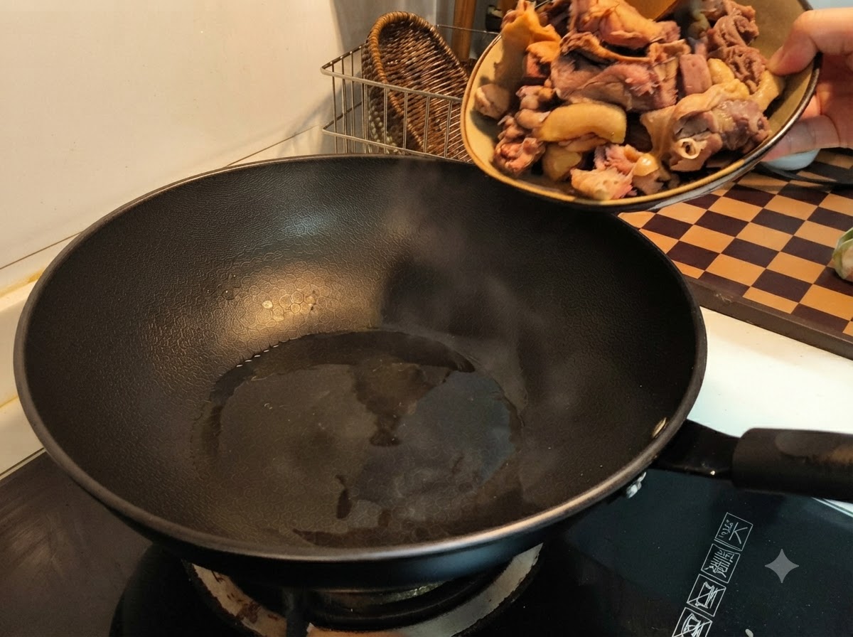 Eine Hand gießt blanchierte Entenstücke von einem Teller in einen heißen schwarzen Wok mit Öl.
