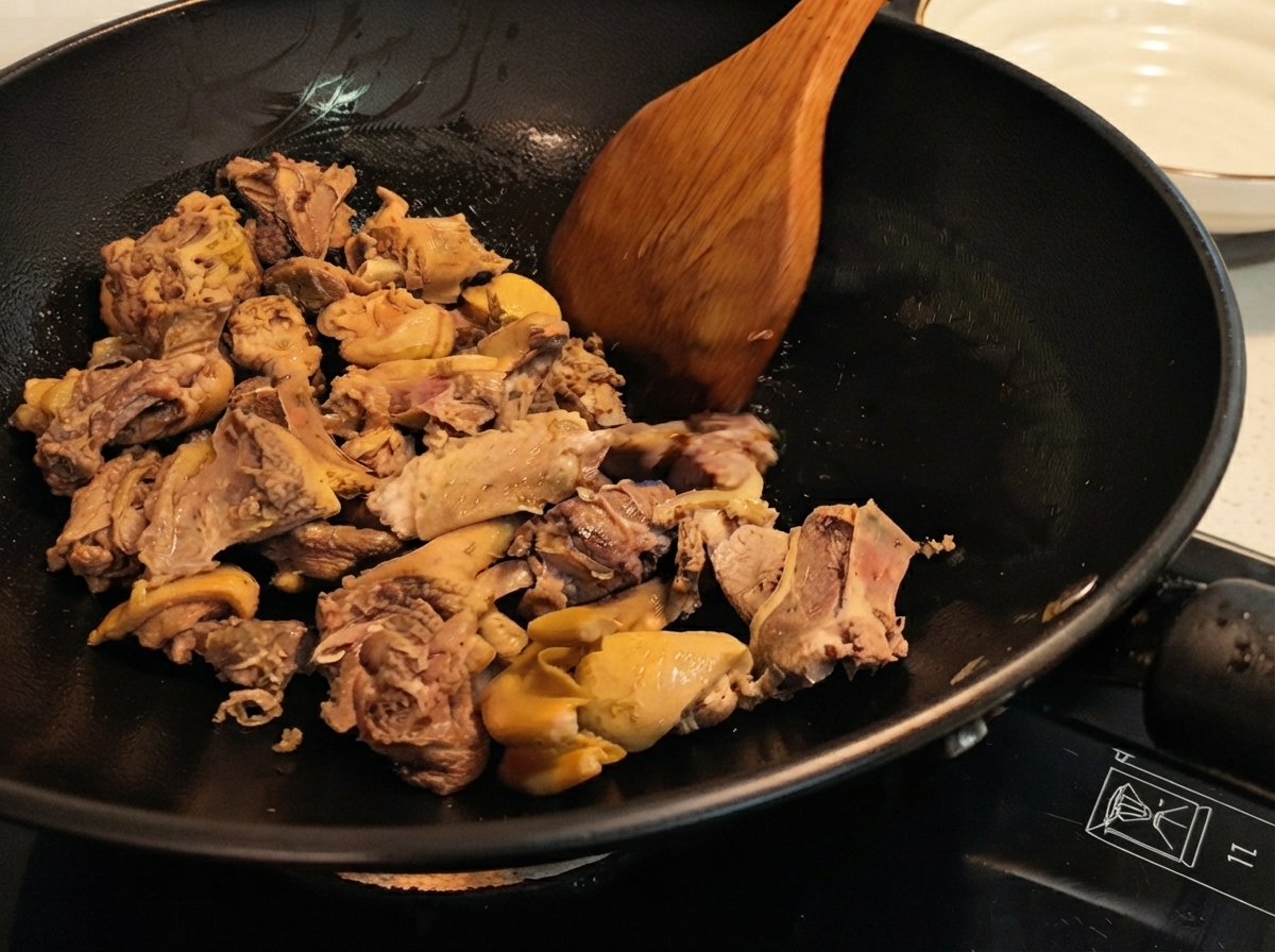 Entenstücke werden mit einem Holzlöffel in einem Wok gewendet, wobei die gebräunte Haut zu sehen ist.