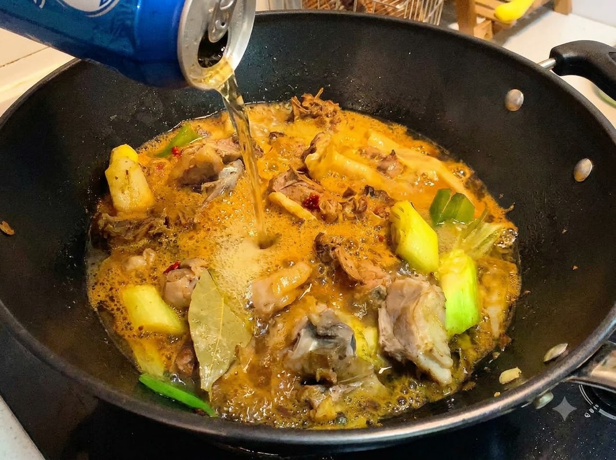 Eine Dose Bier wird in einen Wok mit gekochten Entenstücken und einer reichhaltigen, köchelnden Sauce gegossen.