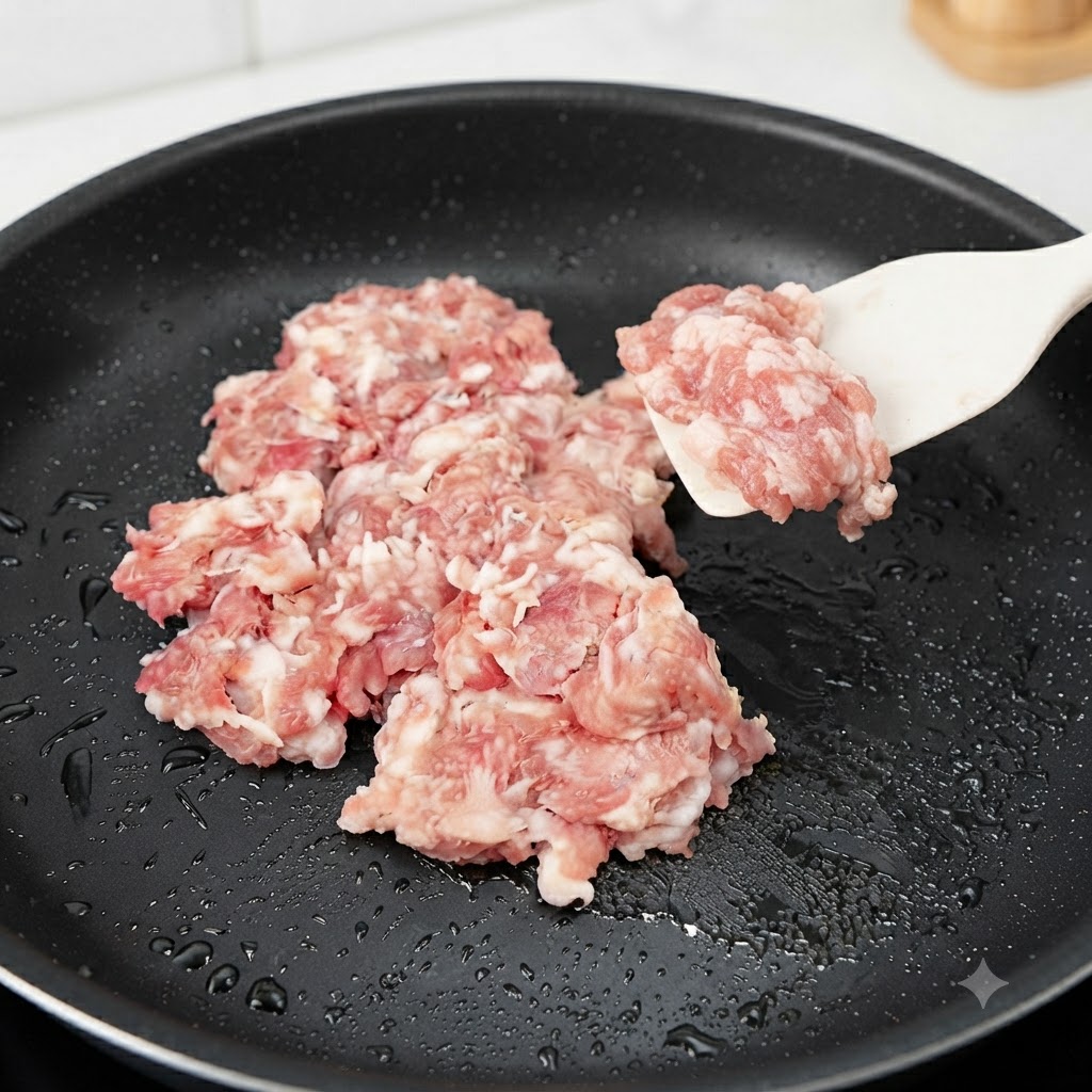 Rohes Hackfleisch wird in einer schwarzen Pfanne mit einem Silikonspatel hinzugefügt und angebraten.